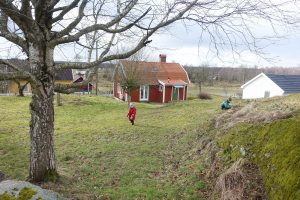 En sluttande gräsmatta nedanför ett berg, längst ner ett rött litet hus.