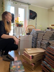 En kvinna sitter på knä på golvet bland högar av böcker.
