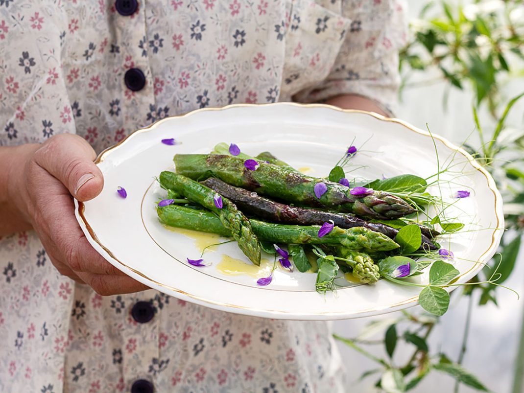 Gröna sparris på ett fat med dressing dekorerad med lila vackra blomblad
