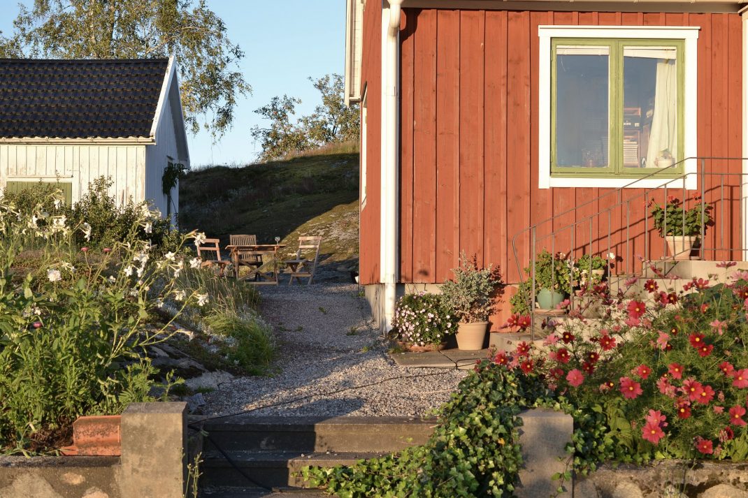 En röd stuga med blommor på trappen. 