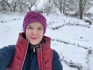 En glad Sara Bäckmo i knalliga färger framför en snötäckt köksträdgård.