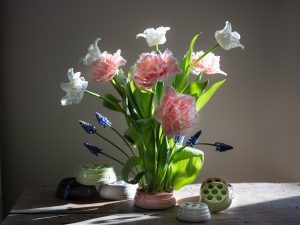 En vacker bukett med tulpaner och blå pärlhyacinterstår fint i en blomhållare i keramik..