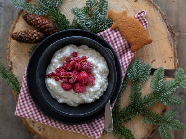 En tallrik med risgrynsgröt toppad med tinade hallon och vinbär. En pepparkaksgris ligger på kanten. Allt serverat i en julig känsla.