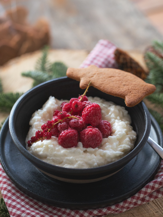 En tallrik med risgrynsgröt toppad med tinade hallon och vinbär. En pepparkaksgris ligger på kanten. Allt serverat i en julig känsla.